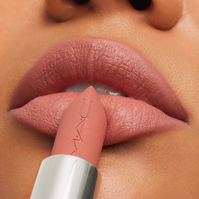 Primer plano de barra de labial mate nude M·A·C Powder Kiss aplicándose sobre los labios con acabado difuminado.