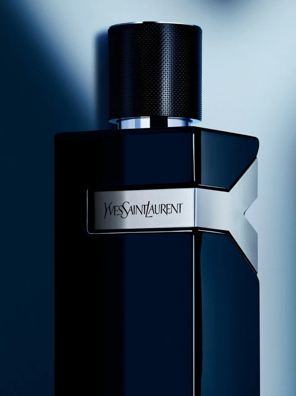 Frasco negro del perfume de hombre Yves Saint Laurent Y con placa plateada sobre fondo con luces azules.