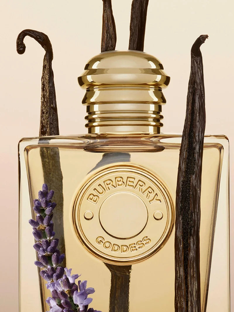 Perfume de mujer Burberry Goddess rodeado de vainas de vainilla y flores de lavanda sobre fondo beige.
