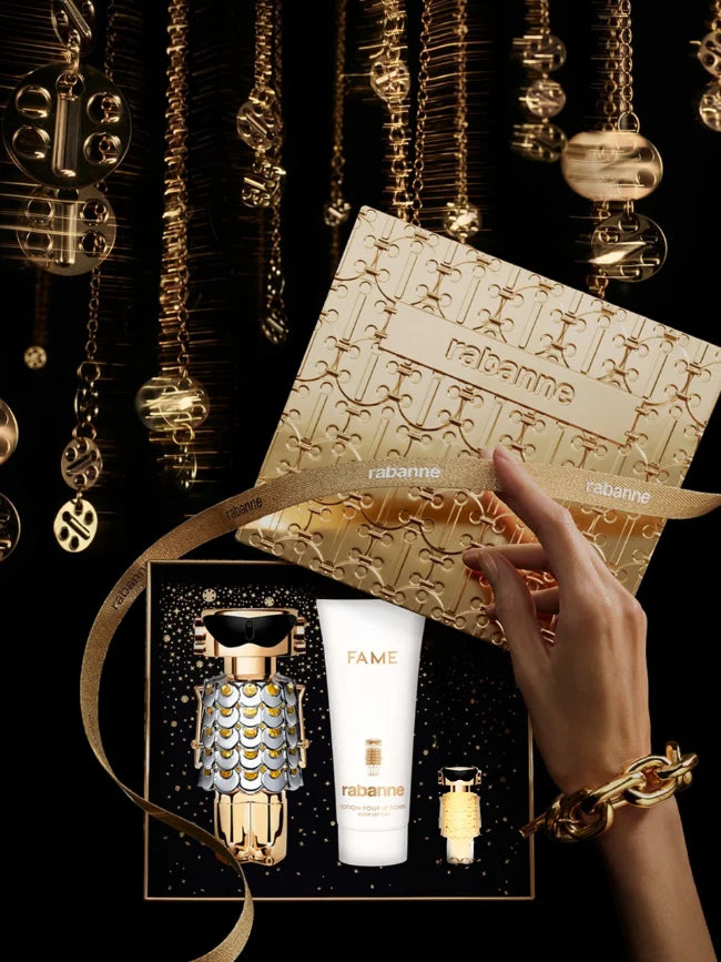 Set de perfume Rabanne Fame para mujer con estuche dorado, loción corporal y miniatura sobre fondo negro.
